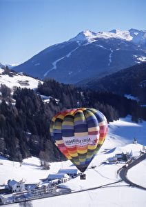 Ein Heißluftballon beim Aufstieg in der verschneiten Winterkulisse des Hochpustertals. (