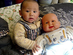 Kleinkind mit chinesischer Puppe, 2009 von Kelsang Tsering (geb. 1969). Traditionell gibt es in Tibet keine speziellen Spielsachen und Puppen für Kinder. Die Babypuppe aus Plastik stammt aus China und wurde wohl ursprünglich für den westlichen Markt hergestellt. (Kelsang Tsering)
