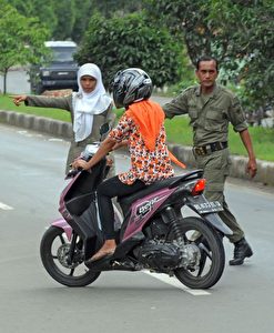 Ein Team der Scharia-Polizei in Banda Aceh, Indonesien, hält eine Motorradfahrerin an einem Kontrollpunkt an, weil sie zu enganliegende Kleidung trägt.  Aceh hat sich von anderen Teilen Indonesiens durch die Einführung der Scharia und der Religionspolizei hervorgehoben.