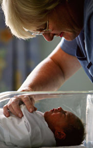 Ein freundlicher Blick der Hebamme auf das Neugeborene in dem Plastikbettchen.