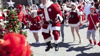 Weihnachtsmänner tanzen um den Christbaum