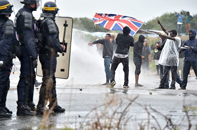 A participant holds up the Union Jack as French anti-riot police fire water canons at participants during a march in support of migrants and refugees in the so-called 'Jungle' camp in the French northern port city of Calais on October 1, 2016. Between 7,000 and 10,000 migrants are currently living in the "Jungle", the launchpad for their attempts to stow away on lorries heading across the Channel to England. Rights groups have criticised the hardship and dangers facing the migrants living in the camp, particularly the hundreds of unaccompanied minors. / AFP / PHILIPPE HUGUEN (Photo credit should read PHILIPPE HUGUEN/AFP/Getty Images)