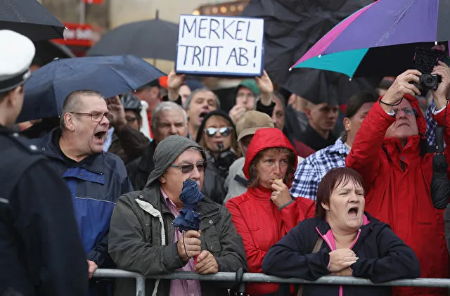 DRESDEN, GERMANY - OCTOBER 03: Angry onlookers, including one holding a sign that reads: &quot;Merkel resign,&quot; shout &quot;Merkel muss weg!&quot; (&quot;Merkel must go!&quot;) and &quot;Volksverraeter!&quot; (&quot;Traitor of the people!&quot;) outside the Semperoper opera house, where German Chancellor Angela Merkel and other leading government members were attending celebrations to mark German Unity Day on October 3, 2016 in Dresden, Germany. Unity Day, called Tag der Deutschen Einheit, commemorates German reunification of East and West Germany following the end of the Cold War. This year's celebrations are being accompanied by protests from both left and right-wing groups, notably the anti-Muslim and anti-immigration Pegida movement, which has its roots in Dresden, as well as extraordinary security measures by police. (Photo by Sean Gallup/Getty Images)