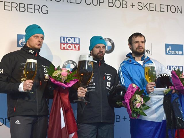 Prost: Tomas Dukurs (l-r, 2. Platz), Martins Dukurs (1. Platz) und Alexander Tretiakov (3. Platz) auf dem Podium. Foto: Caroline Seidel/dpa