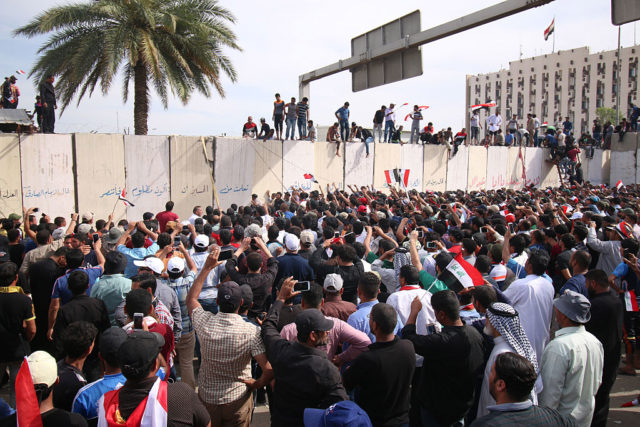 Iraqi protesters climb over a concrete wall surrounding the parliament (unseen) after breaking into Baghdad's heavily fortified "Green Zone" on April 30, 2016. Thousands of angry protesters broke into Baghdad's Green Zone and stormed the parliament building after lawmakers again failed to approve new ministers. Jubilant supporters of cleric Moqtada al-Sadr invaded the main session hall, shouting slogans glorifying their leader and claiming that they had rooted out corruption. / AFP / HAIDAR MOHAMMED ALI (Photo credit should read HAIDAR MOHAMMED ALI/AFP/Getty Images)