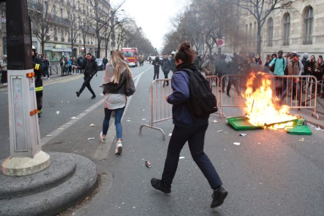 People run past a burning dustbin as students protest against police brutality, following the alleged rape of Theo, outside the "Lycee Voltaire" secondary school in Paris, on February 23, 2017. / AFP / GEOFFROY VAN DER HASSELT (Photo credit should read GEOFFROY VAN DER HASSELT/AFP/Getty Images)