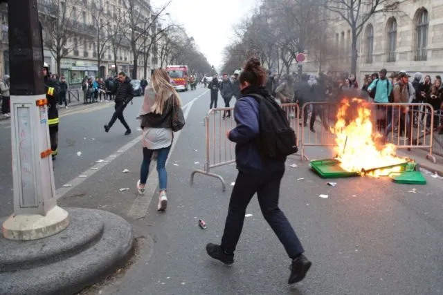 People run past a burning dustbin as students protest against police brutality, following the alleged rape of Theo, outside the &quot;Lycee Voltaire&quot; secondary school in Paris, on February 23, 2017. / AFP / GEOFFROY VAN DER HASSELT (Photo credit should read GEOFFROY VAN DER HASSELT/AFP/Getty Images)