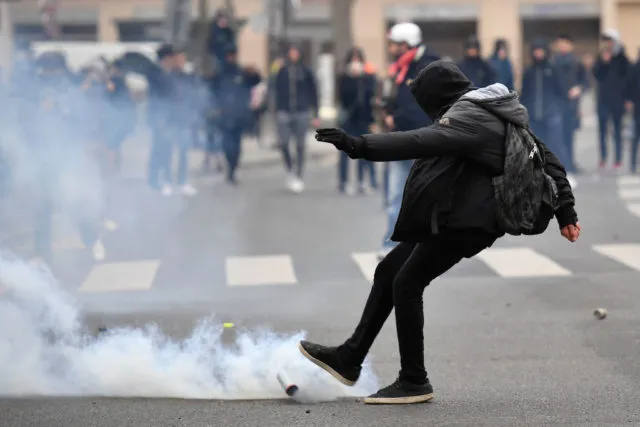 A man kicks away a smoke grenade launched by riot police during a protest of students against police brutality, following the alleged rape of Theo, next to the &quot;Lycee Voltaire&quot; secondary school in Paris, on February 23, 2017. / AFP / Lionel BONAVENTURE (Photo credit should read LIONEL BONAVENTURE/AFP/Getty Images)