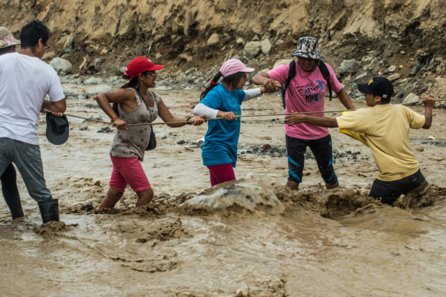Local residents try to cross a flash flood in Huachipa district, on the east side of Lima, on March 19, 2017. El Nino-fuelled flash floods and landslides hit parts of Lima, where most of the water distribution systems have collapsed due to unusual heavy seasonal downpours and people are facing drinking water shortages. / AFP PHOTO / ERNESTO BENAVIDES (Photo credit should read ERNESTO BENAVIDES/AFP/Getty Images)