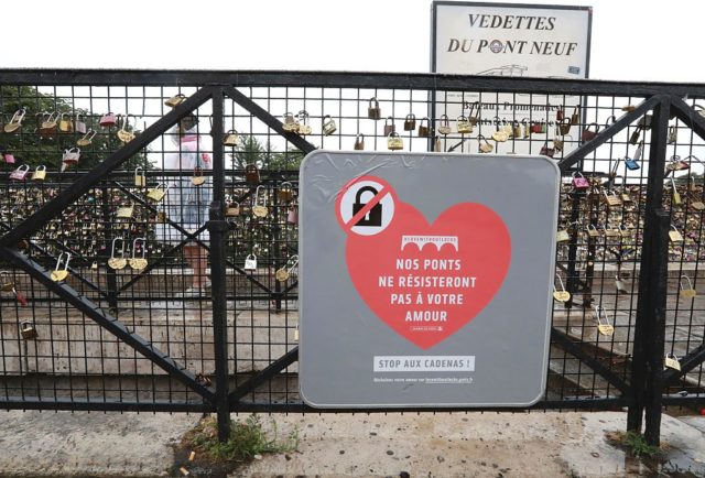 A placard reading "our bridges won't resist your love", is seen among "love-locks" hung on the bridge of Pont Neuf in Paris, on August 4, 2016. Love may know no bounds, but Paris intends to instill some: authorities are going to take a tougher line with swooning couples attaching "love-locks" to city bridges as a sign of their undying devotion. In June last year authorities removed hundreds of thousands of such padlocks from the city bridges, notably the Pont des Arts which had a section collapse under the weight of the locks. / AFP / JACQUES DEMARTHON (Photo credit should read JACQUES DEMARTHON/AFP/Getty Images)