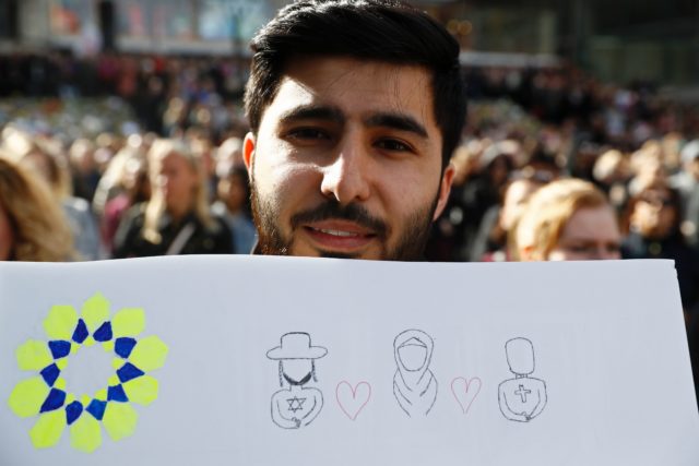 A man holds up a sign featuring symbols of different religions during a memorial ceremony at Sergels Torg plaza in Stockholm, Sweden on April 9, 2017 close to the point where a truck drove into a department store two days before. / AFP PHOTO / Odd ANDERSEN (Photo credit should read ODD ANDERSEN/AFP/Getty Images)