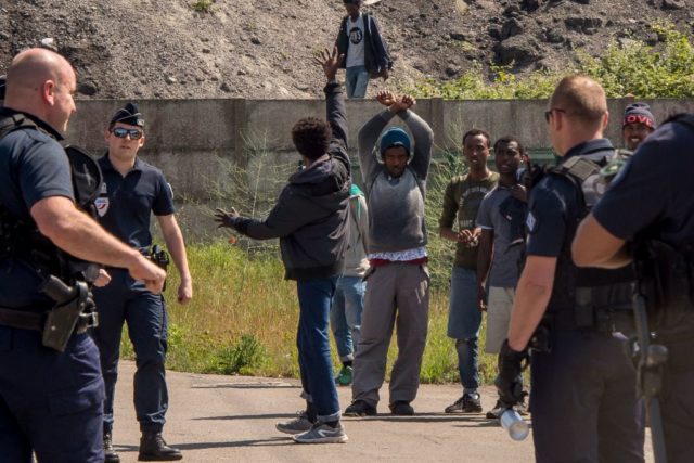 Migrants raise their arms in front of a French police officer on June 1, 2017, in Calais. Migrants set brushwoods on fire on the A16 highway late on May 31, 2017, near Calais, northern France. / AFP PHOTO / PHILIPPE HUGUEN (Photo credit should read PHILIPPE HUGUEN/AFP/Getty Images)