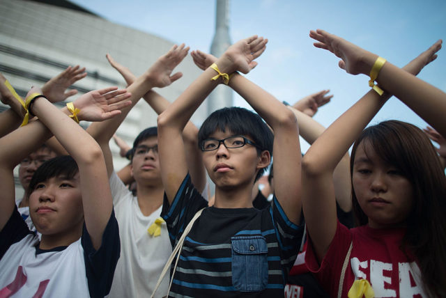 HONG KONG - OCTOBER 01: Student pro-democracy group Scholarism convenor Joshua Wong (C) makes a gesture at the Flag Raising Ceremony at Golden Bauhinia Square on October 1, 2014 in Hong Kong. Thousands of pro democracy supporters continue to occupy the streets surrounding Hong Kong's Financial district. Protest leaders have set an October 1st deadline for their demands to be met and are calling for open elections and the resignation of Hong Kong's Chief Executive Leung Chun-ying. (Photo by Anthony Kwan/Getty Images)