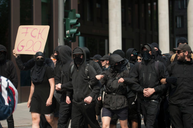 Hooded protessters march with a placard reading "FCK G20" during a protest on July 7, 2017 in Hamburg, northern Germany, where leaders of the world's top economies gather for a G20 summit. Protesters clashed with police and torched patrol cars in fresh violence ahead of the G20 summit, police said. German police and protestors had clashed already on Thursday (July 6, 2017) at an anti-G20 march, with police using water cannon and tear gas to clear a hardcore of masked anti-capitalist demonstrators, AFP reporters said. / AFP PHOTO / STEFFI LOOS (Photo credit should read STEFFI LOOS/AFP/Getty Images)