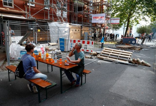 Local residents have installed a a table with drinks while protesters of the black block run away from teargas in the background on July 7, 2017 in Hamburg, northern Germany, where leaders of the world's top economies gather for a G20 summit. Protesters clashed with police and torched patrol cars in fresh violence ahead of the G20 summit, police said. German police and protestors had clashed already on Thursday (July 6, 2017) at an anti-G20 march, with police using water cannon and tear gas to clear a hardcore of masked anti-capitalist demonstrators, AFP reporters said. / AFP PHOTO / Odd ANDERSEN (Photo credit should read ODD ANDERSEN/AFP/Getty Images)