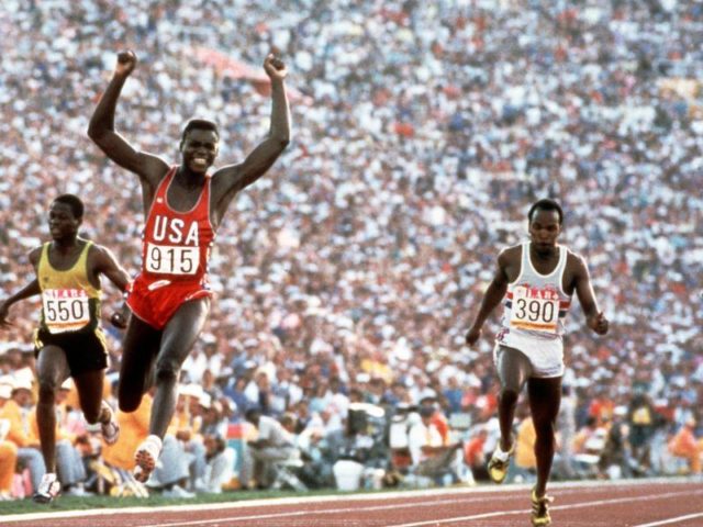 Carl Lewis (M) reißt die Arme hoch, nachdem er in Los Angeles 1984 mit 9,99 Sekunden über 100 Meter gewinnt. Foto: dpa/dpa