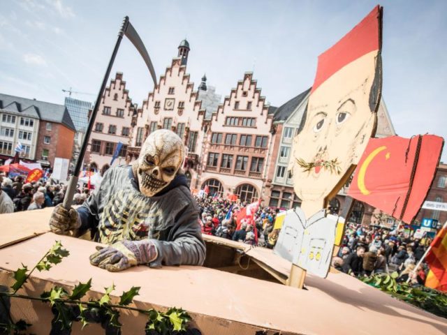 Ein als Tod verkleideter Demonstrant steht auf dem Frankfurter Römerberg auf einem Leopard-Panzer aus Pappe neben einem Bildnis des türkischen Präsidenten Erdogan. Foto: Frank Rumpenhorst/dpa