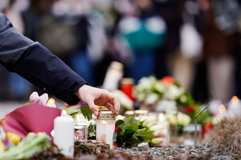 Menschen haben vor einem Gebäude der Heidelberger Universität Blumen und Kerzen niederlegt.