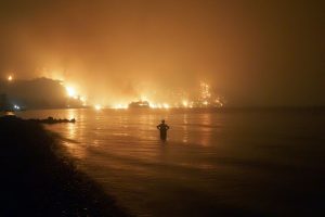 Ein Mann beobachtet, wie sich Waldbrände dem Strand von Kochyli in der Nähe des Dorfes Limni auf der Insel Evia (Griechenland) nähern.