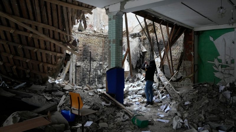 Eine Frau fotografiert ein zerstörtes Unterkunftsgebäude in der Nähe eines Kontrollpunktes in Brovary.