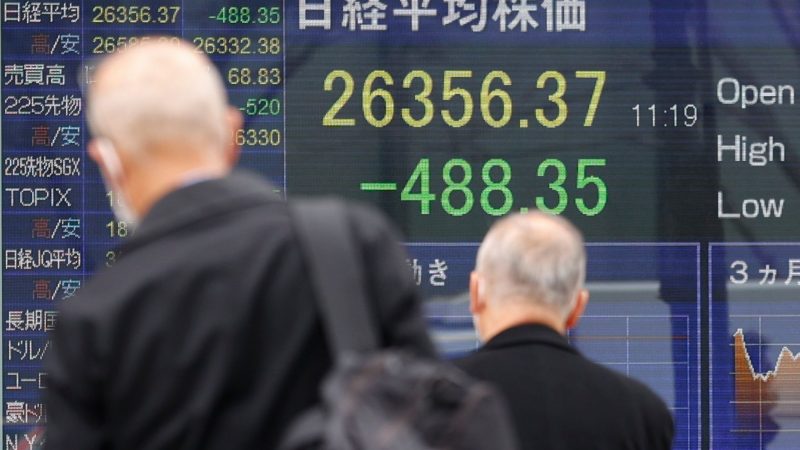 Menschen mit Mund-Nasen-Schutz gehen an einer elektronischen Börsentafel vorbei, die den japanischen Nikkei-Aktienindex anzeigt.