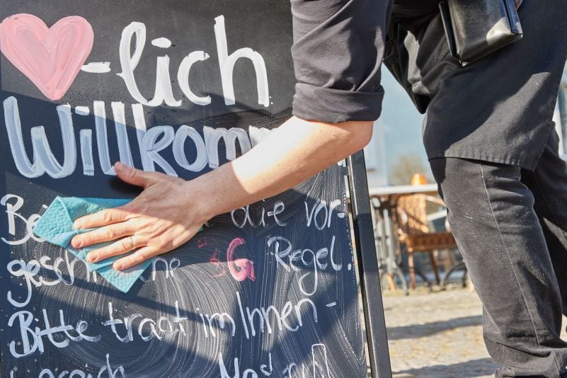Kellner Tonet Devolli vom Restaurant Mühlstein in Wedel beseitigt die Hinweise zu den 3G-Regeln.