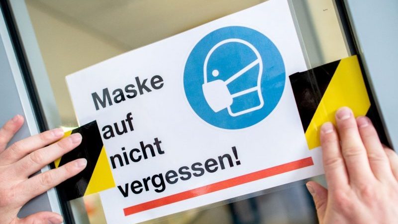 Der Hausmeister des Neuen Gymnasiums in Oldenburg klebt ein Schild mit der Aufschrift «Maske auf nicht vergessen!» an die Glasscheibe einer Zwischentür.
