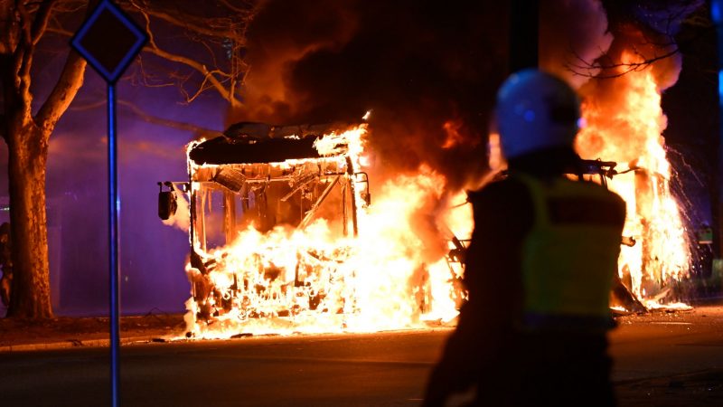 Bereitschaftspolizisten stehen vor einem brennenden Stadtbus.