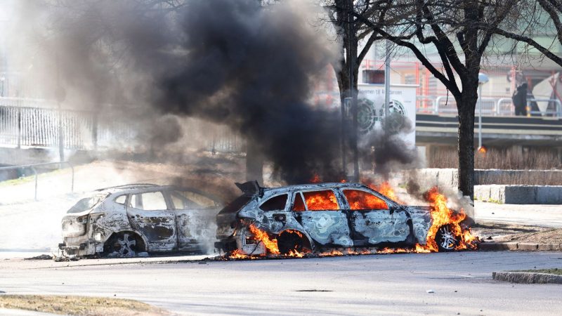 Zwei Autos stehen auf einem Parkplatz in Norrköping während der Ausschreitungen in Flammen.