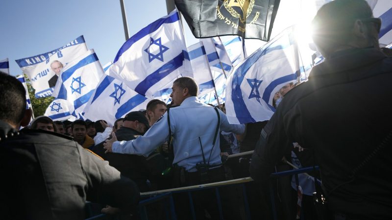 Ein israelischer Polizeibeamter steht vor rechten Aktivisten, die sich zu einem Flaggenmarsch in der Altstadt von Jerusalem versammelt haben.