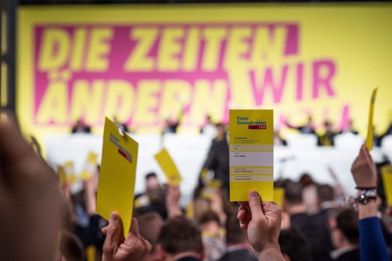 Delegierte halten beim ersten Präsenzparteitag der FDP nach dem Beginn von Corona die Stimmkarten hoch.
