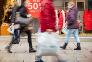 Menschen an einem Rabattschild vorbei. Viele Verbraucher in Deutschland halten sich zu Jahresbeginn aus Skepsis über die wirtschaftliche Entwicklung weiter zurück.