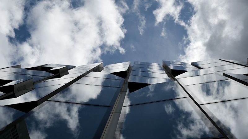 Weiße Wolken und blauer Himmel spiegeln sich in der Glasfassade des Gebäudes der DWS Group.