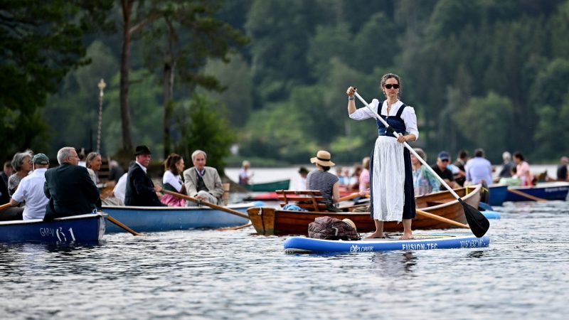Auf einem Stand-up-Board nimmt eine Frau im Dirndl an einer Fronleichnamsprozession auf dem Staffelsee in Oberbayern teil.