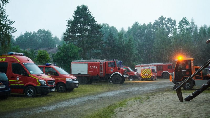 Starker Regen prasselt auf Rettungsfahrzeuge von Feuerwehr und THW nahe Treuenbrietzen. Die Niederschläge helfen den Brandbekämpfern.