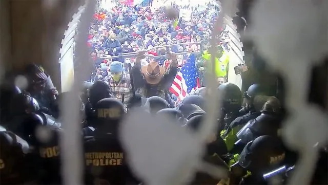 Luke Coffee hält eine Krücke hoch, als er in der Lücke zwischen der Polizei und der Menge am Lower West Terrace Tunnel steht. „Im Namen Jesu, bitte hört auf!“, sagte er.