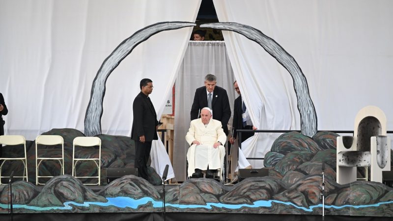 Papst Franziskus wird in seinem Rollstuhl auf die Bühne geschoben.