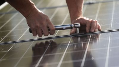 Ein Arbeiter montiert Photovoltaikmodule auf dem Dach eines Wohnhauses.