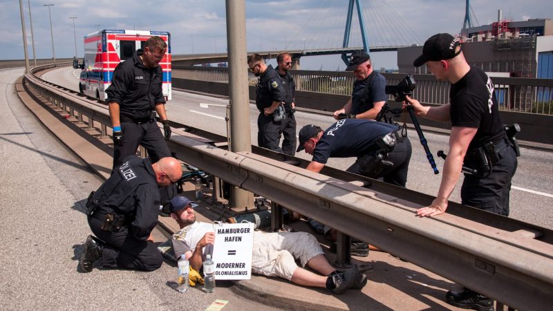 Polizisten versuchen auf der Köhlbrandbrücke zwei mit einem Eisenrohr miteinander verbundene Klimaaktivisten zu lösen.