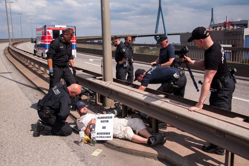 Polizisten versuchen auf der Köhlbrandbrücke zwei mit einem Eisenrohr miteinander verbundene Klimaaktivisten zu lösen.