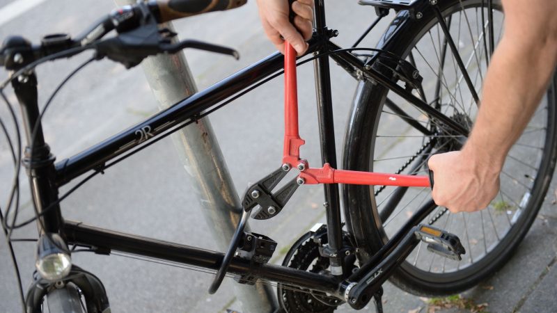 Ein Mann versucht mit einem Bolzenschneider, ein Fahrradschloss aufzubrechen (gestellte Szene).