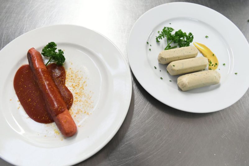 Eine vegane Currywurst und vegane Weißwürste liegen auf Tellern an der Essensausgabe im Hofbräuzelt auf dem Oktoberfest.