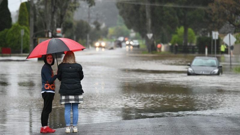 Menschen stehen an einer überschwemmten Straße in Melbourne.
