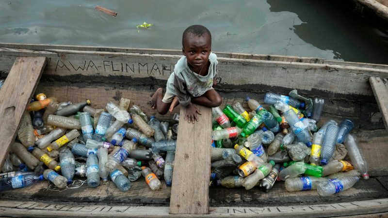 Ein kleines Kind sitzt in einem Kanu zwischen leeren Plastikflaschen, die im schwimmenden Slum von Makoko in Nigeria gesammelt wurden. Schätzungsweise 100.000 Menschen leben hier unter schlechtesten Bedingungen.