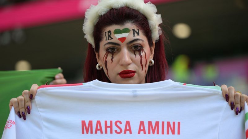Eine Frau aus dem Iran hält vor dem Fußball-WM-Spiel zwischen Wales und dem Iran in Katar ein Trikot mit der Aufschrift der verstorbenen iranischen Kurdin "Mahsa Amini". Der Tod von Mahsa Amini hat anhaltende, landesweite Proteste im Iran ausgelöst.