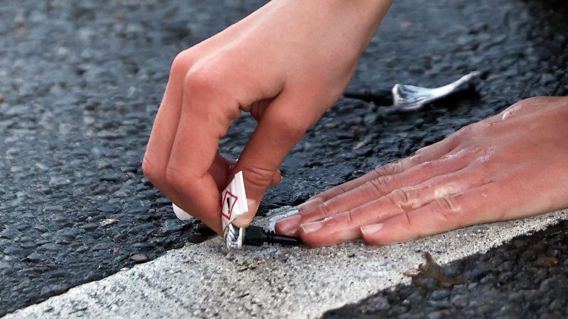 Ein Aktivist von «Letzte Generation» klebt seine Hand mit Sekundenkleber auf der Straße in Berlin während einer Sitzblockade fest.