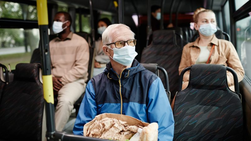 Ein älterer Mann und weitere Passagiere mit Maske im Bus (Foto: SeventyFour/iStock)
