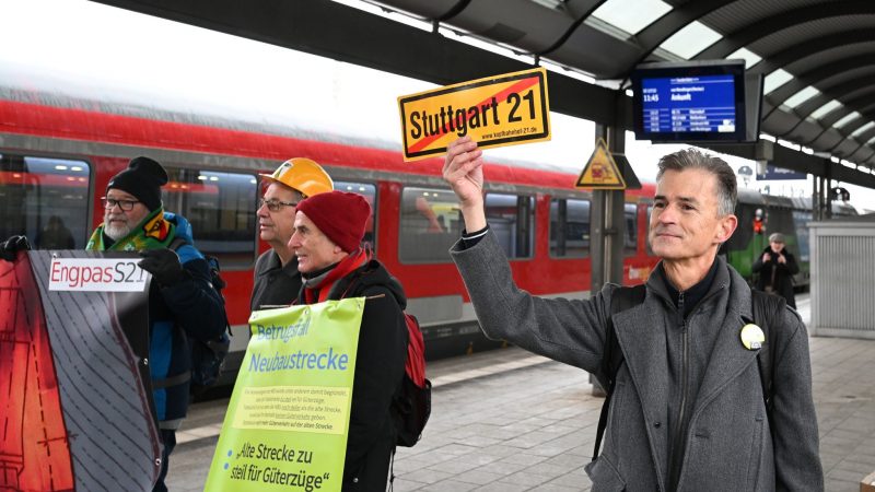 Gegner des milliardenschweren Bahnprojekts Stuttgart 21 stehen vor der feierlichen Eröffnung der Neubaustrecke Wendlingen-Ulm mit Plakaten auf dem Bahnhof in Ulm.