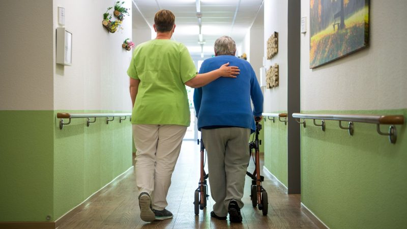 Eine Pflegefachkraft geht mit einer Bewohnerin durch ein Seniorenheim im niedersächsischen Nienburg.