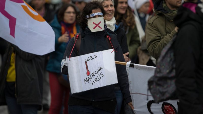 Eine Teilnehmerin einer Demonstration gegen Frankreichs umstrittene Rentenreform mit einem und dem Wortspiel «Macrona Virus» (Archivbild).